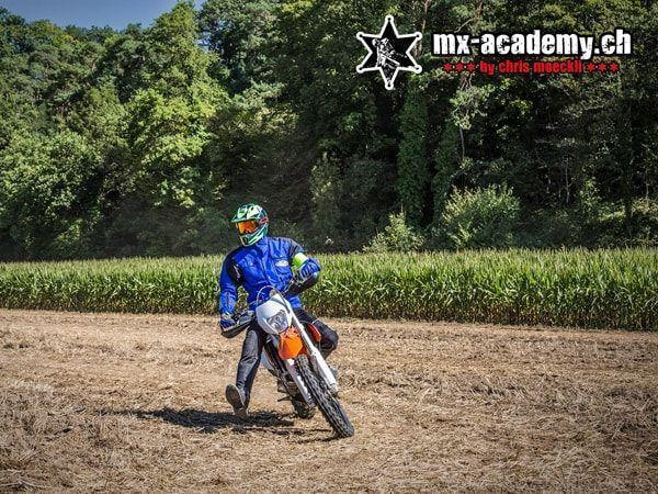 Auszeit vom Alltag: Fahrer in blauer Jacke auf einem orangen Motorrad, gleich daneben ein Maisfeld