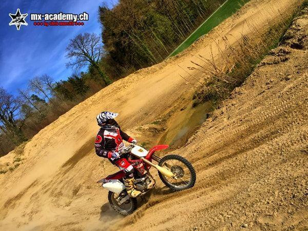 Junger Fahrer legt seine Honda in eine Sandkurve, schräg von der Seite aufgenommen – Jugend Motocross