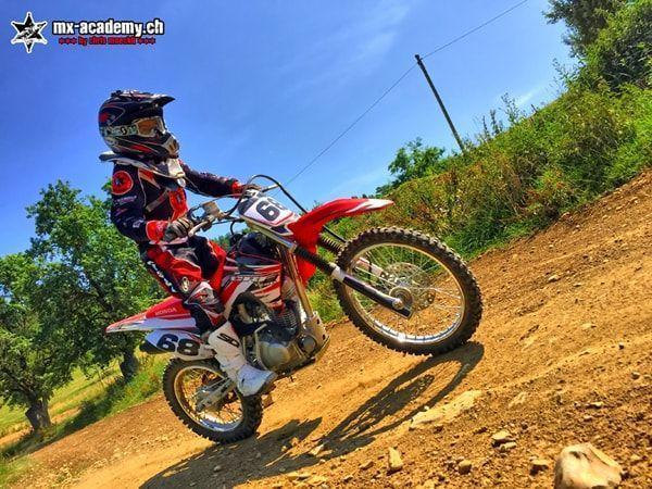 Junger Fahrer mit Startnummer 68 hebt am Hang das Vorderrad seiner Honda – Motocross für Jugendliche