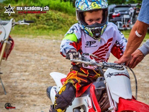 Kind mit buntem Helm sitzt auf einer roten Honda, ein Erwachsener hilft ihm am Motorrad