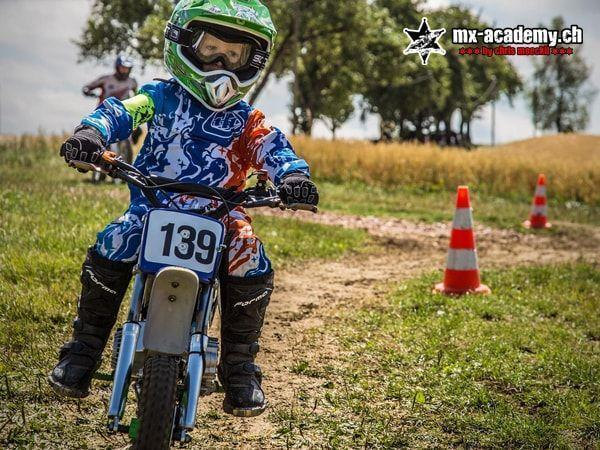 Kinder Motocross: Kind mit Startnummer 139 sitzt auf einem blauen Kindermotorrad, hinten Pylonen