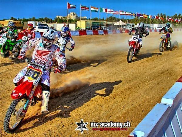 Motorsport Wochenende: mehrere Fahrer starten auf einer Sandstrecke, dahinter Fahnen vieler Länder