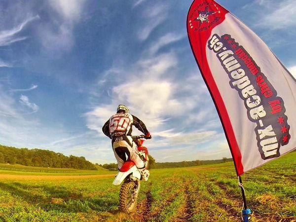 Motocross fahren auf der Wiese: Fahrer mit Startnummer 50 von hinten, daneben eine MX-Academy-Fahne