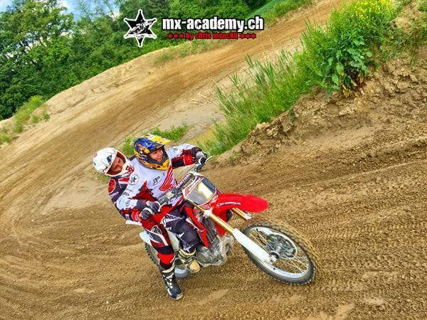 Motocross fahren zu zweit: Zwei Fahrer teilen sich in der Steilkurve eine rote Honda mit der Startnummer 1