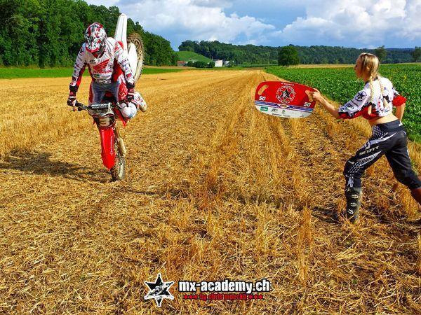 Motocross Technik: Der Fahrer bringt die Honda aufs Vorderrad, während eine Helferin eine Tafel mit der 50 hält