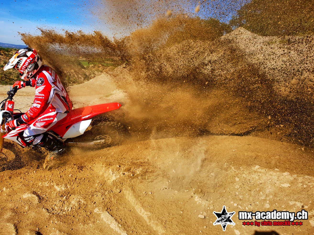 Motocross in der Sandkurve: hinter dem Motorrad steigt eine hohe Fontäne aus Sand auf