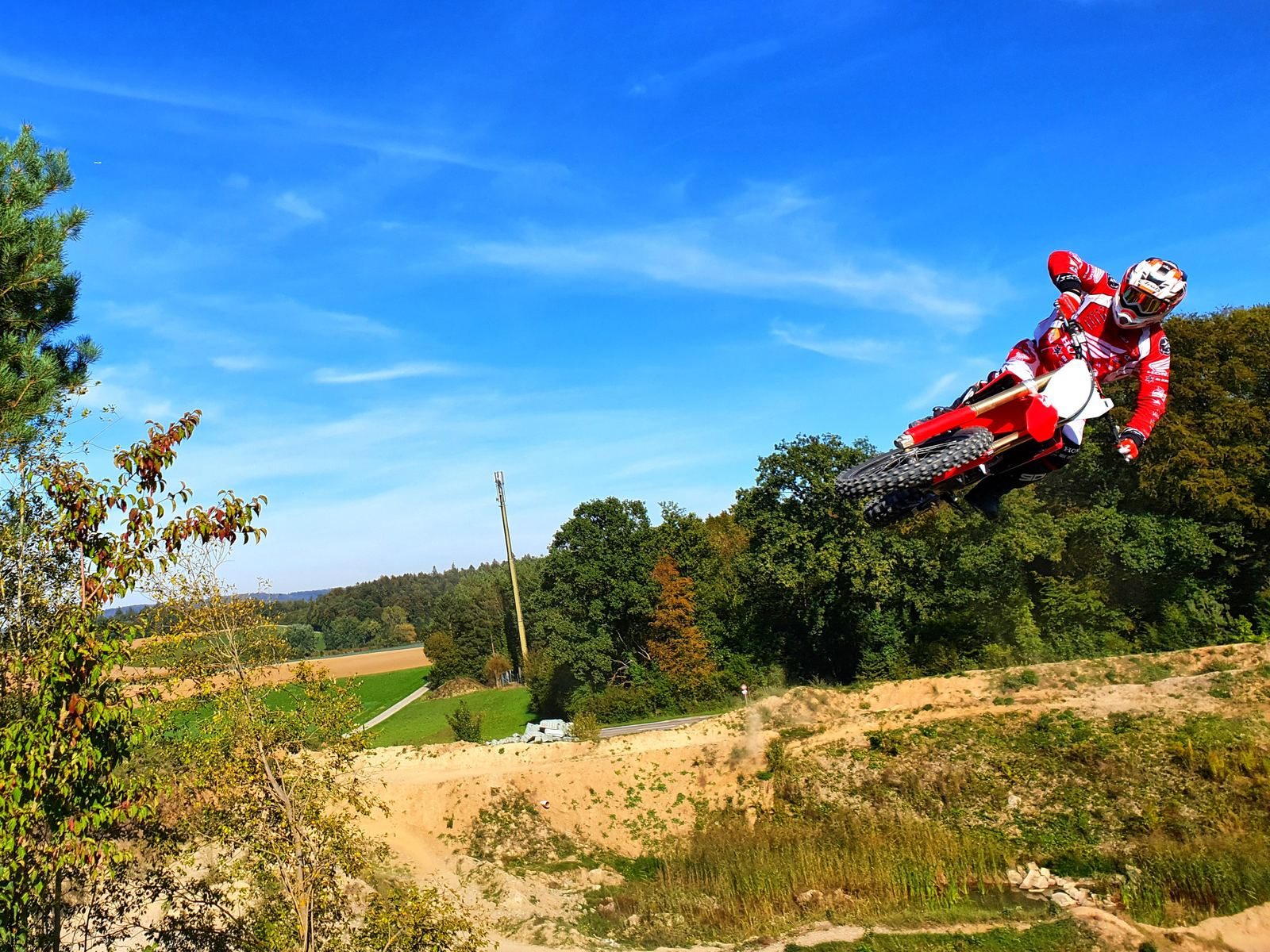 Motocross Sprung unter blauem Himmel: Fahrer fliegt hoch über die grüne Landschaft