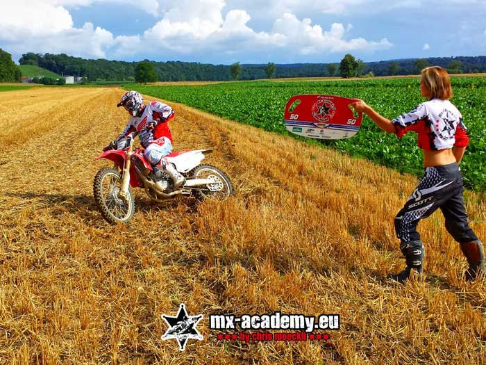 Fahrerin startet, während eine Helferin die Fahne hält – Start beim Supermoto fahren lernen im Gelände